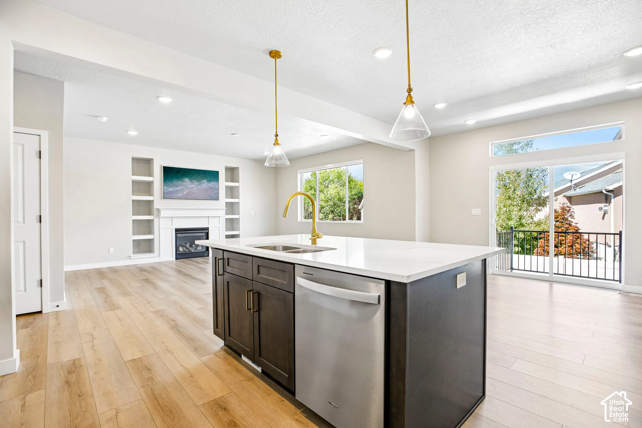 Kitchen island with integrated sink and dishwasher, wood-finish flooring, recessed lighting, and a sliding glass door leading to a balcony with black railings
