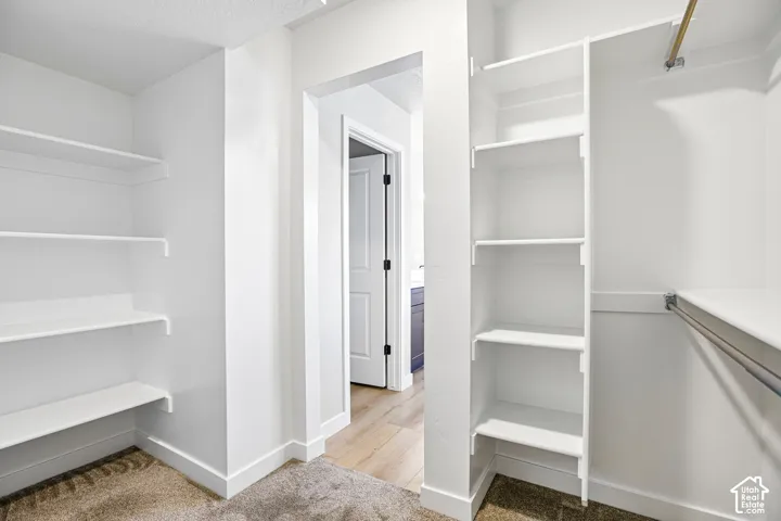 Built-in shelving, hanging rods, light wood-finish flooring, white paneled door, and dark cabinet