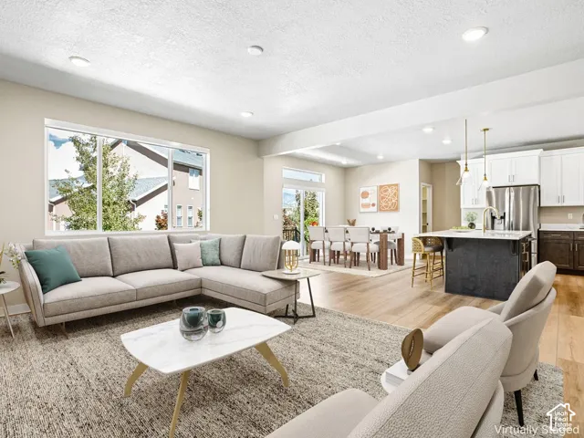 Open-concept living space featuring wood-finish flooring, recessed lighting, a kitchen island with seating, a sliding glass door, and large windows