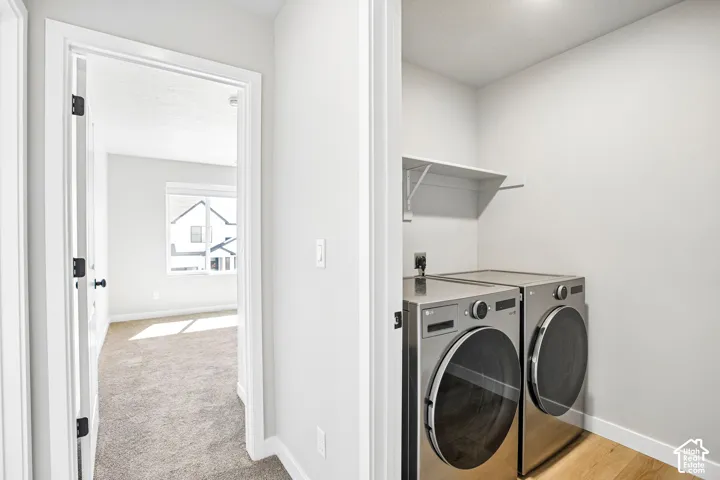 Dedicated laundry area featuring front-loading appliances, an overhead storage shelf, and wood-finish flooring