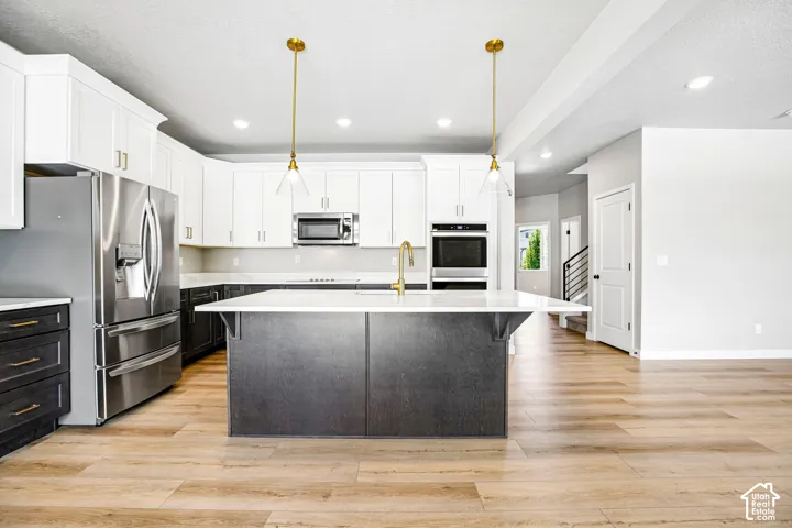Spacious kitchen featuring an expansive center island, stainless steel appliances, dual-tone cabinetry, recessed lighting, and wood-finish flooring