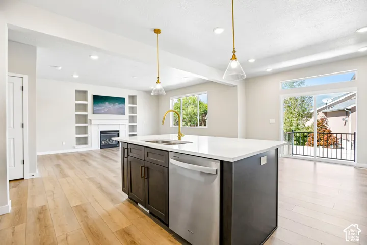 Kitchen island with integrated sink and dishwasher, wood-finish flooring, recessed lighting, and a sliding glass door leading to a balcony with black railings