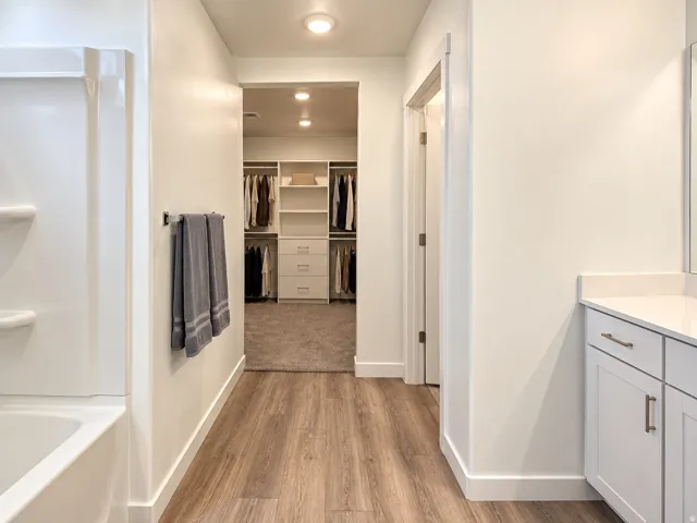 Wood-finish flooring leading to a walk-in closet with built-in shelving and drawers