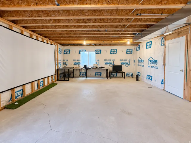 Unfinished basement space featuring exposed wood joists and subfloor, concrete flooring, a white interior door, and a large projection screen