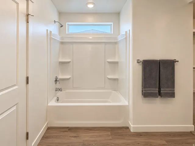 White tub and shower combination with chrome fixtures, integrated shelving, and a transom window