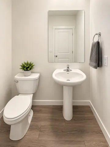 Pedestal sink with chrome faucet, wall-mounted mirror, and wood-finish flooring