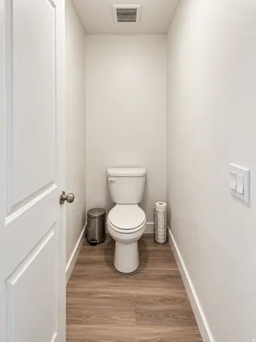 Wood-finish flooring with white trim and a white door with brushed nickel hardware