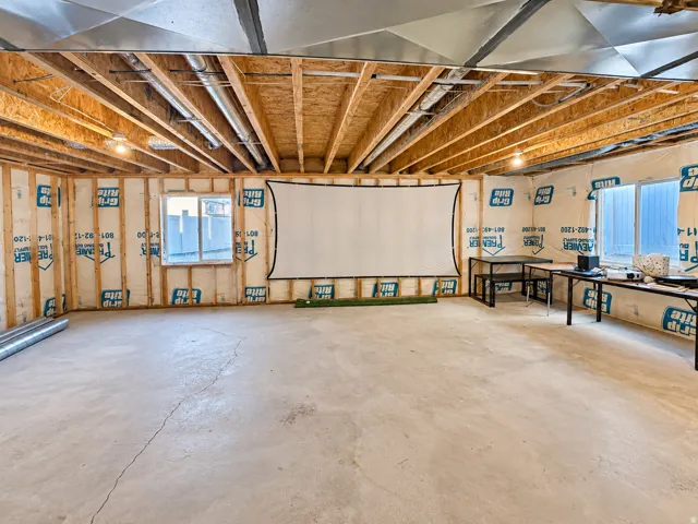 Unfinished basement with exposed wood framing, concrete flooring, and multiple windows