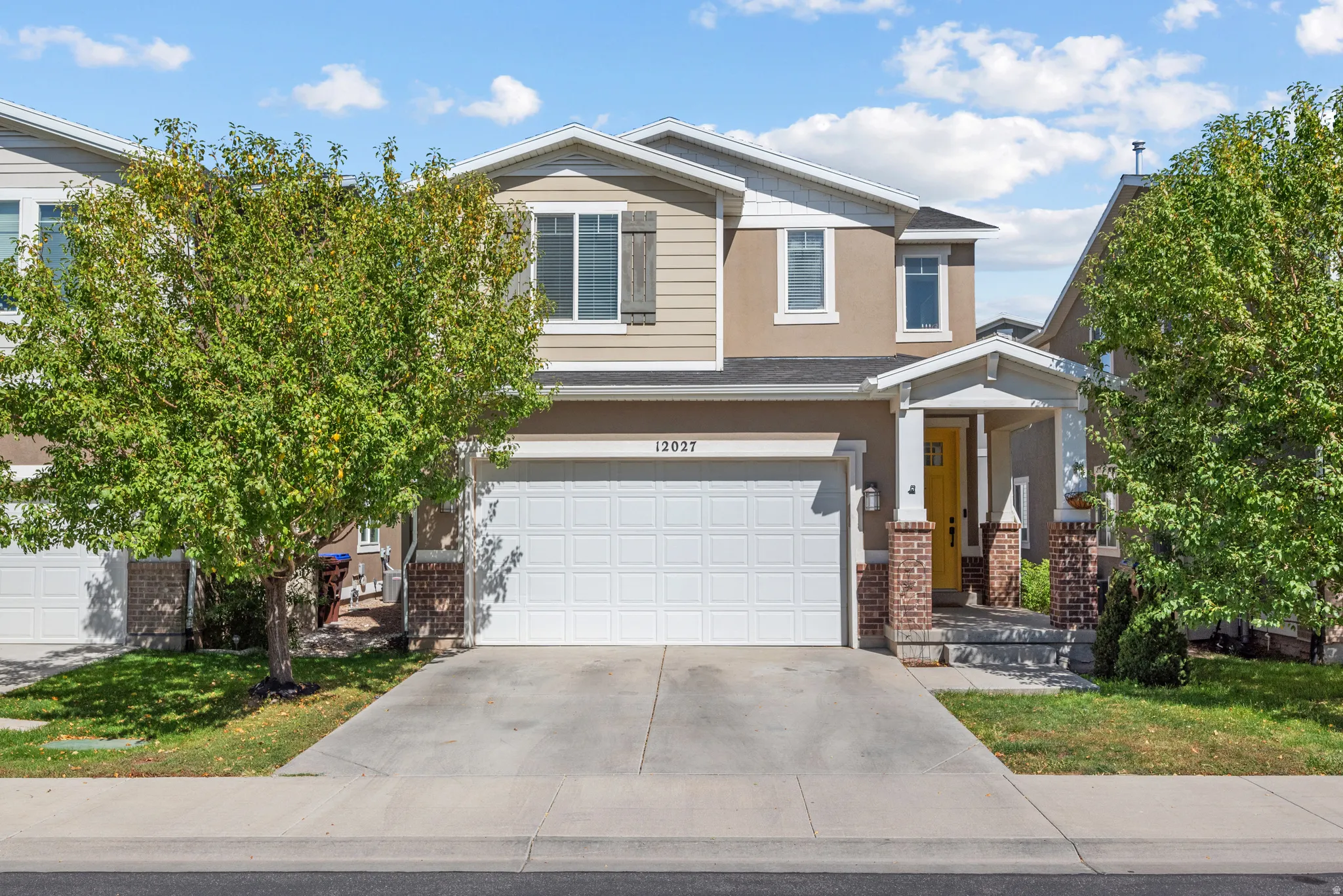 Two-story stucco and siding exterior with an attached garage, covered entryway, brick-clad columns, and a concrete driveway