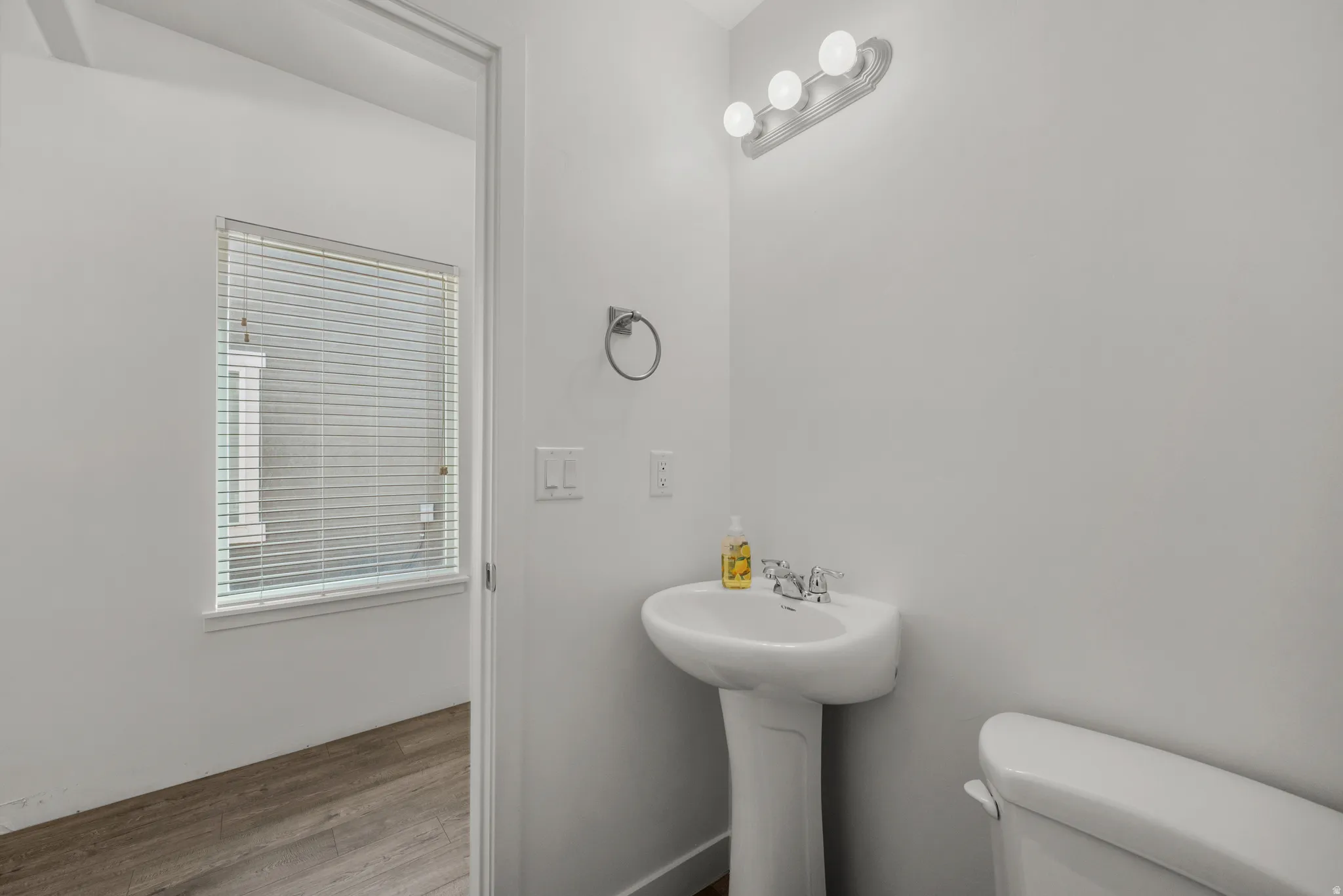 Pedestal sink with chrome faucet, wall-mounted light fixture, and window with horizontal blinds