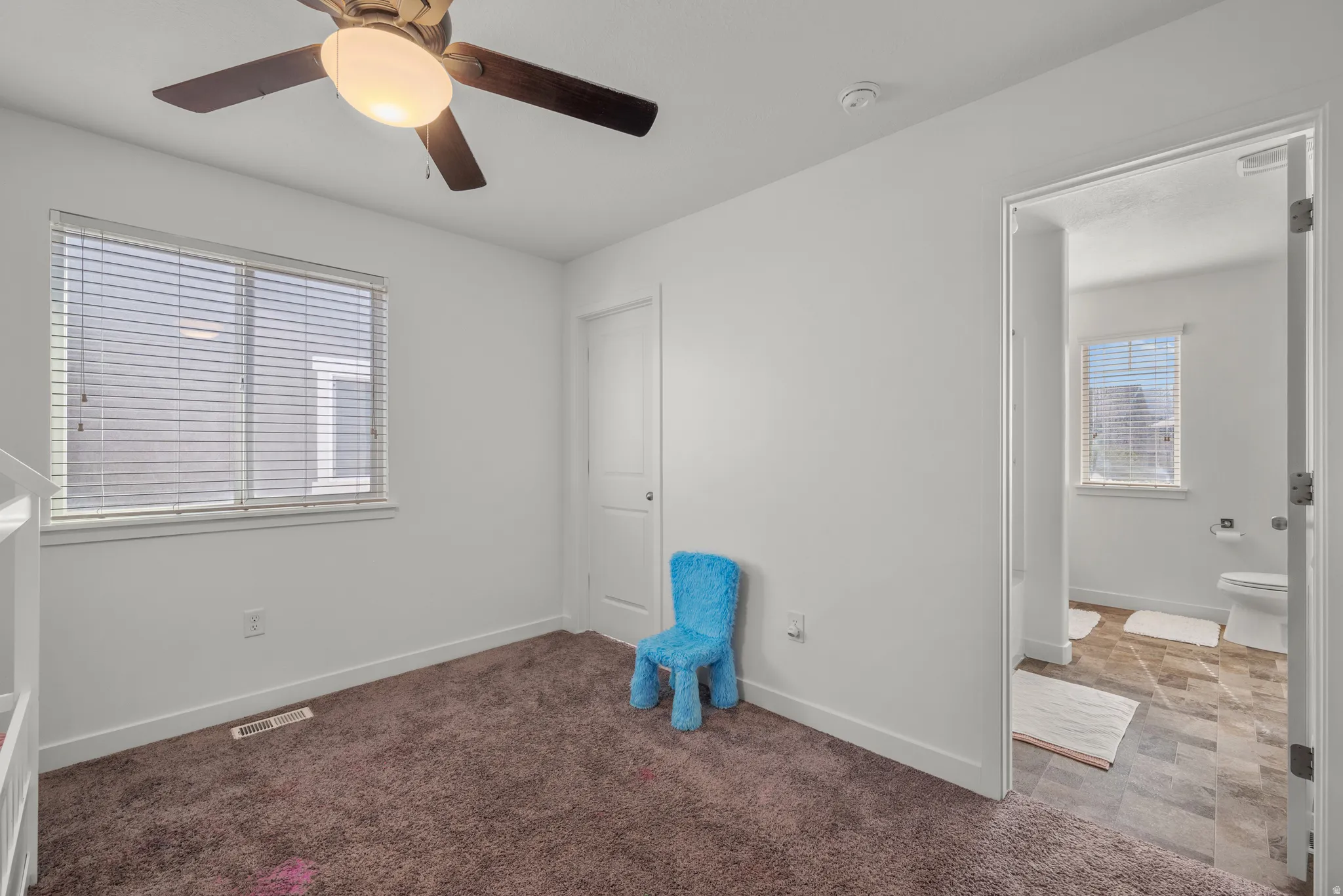 Recessed lighting, wood-finish ceiling fan, window with blinds, brown carpeting, and an adjoining room with tile flooring