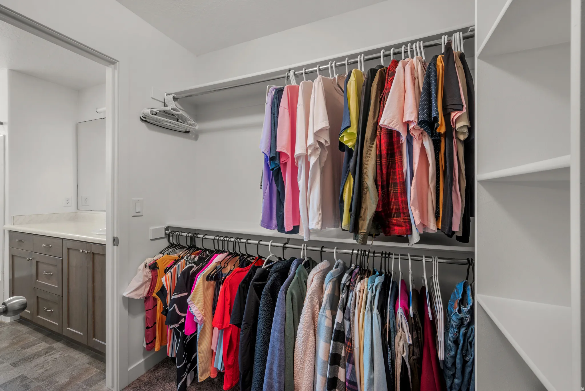 Custom closet with dual hanging rods, built-in shelving, and direct access to a bathroom featuring a vanity with shaker-style cabinetry and a light-toned countertop