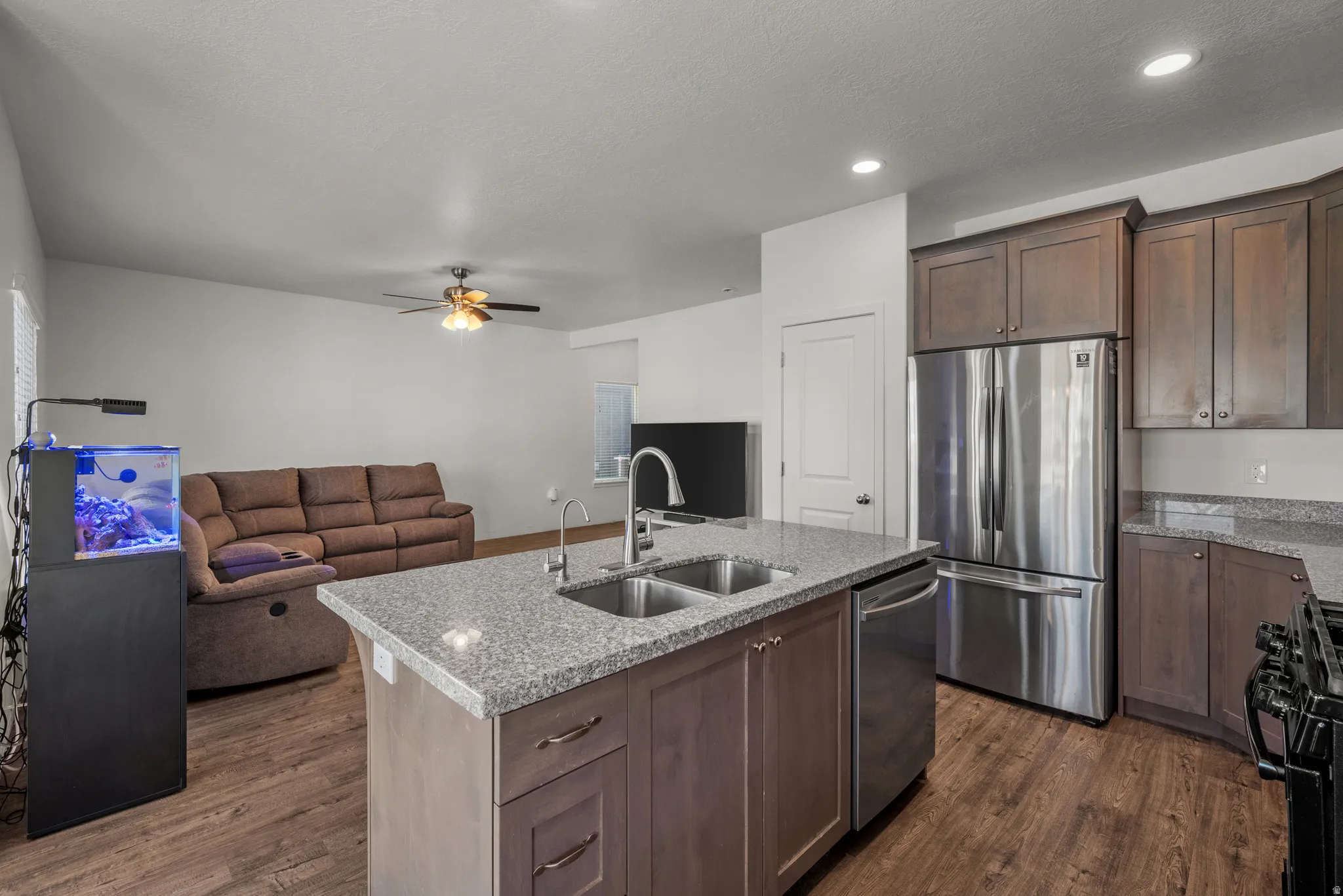 Kitchen island with a double basin sink, stainless steel appliances, wood-finish flooring, recessed lighting, and a ceiling fan