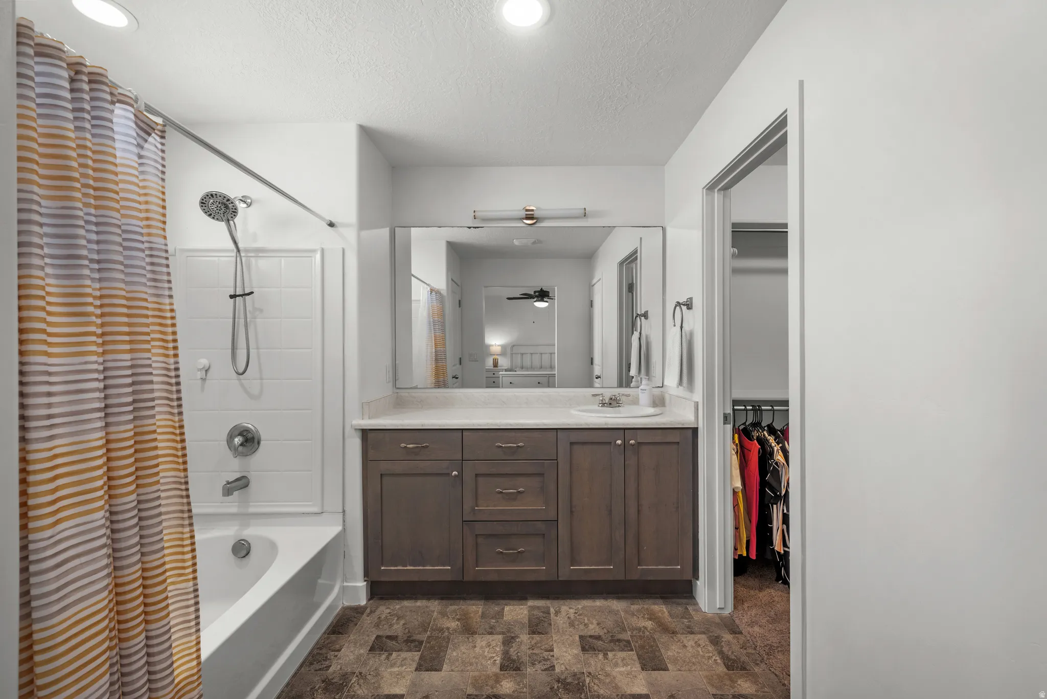 Bathroom featuring a vanity with dark wood-finish cabinetry, a large mirror, a shower-over-tub combination with white subway tile surround, and recessed lighting