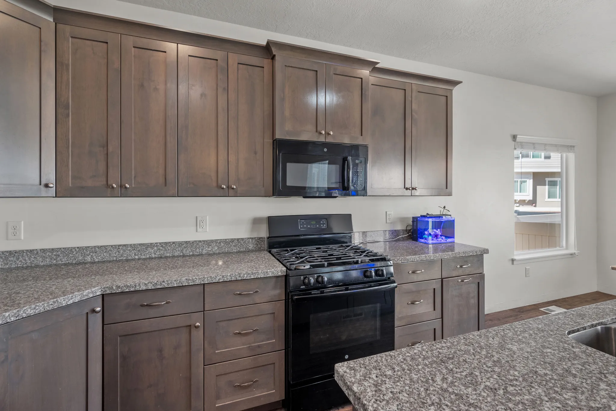 Kitchen featuring wood-finish cabinetry, speckled countertops, a built-in microwave, and a gas range