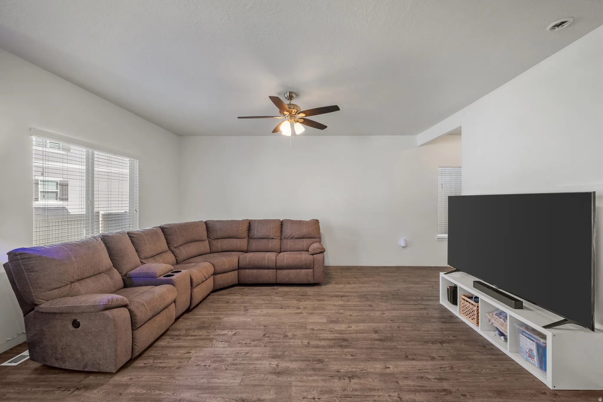 Spacious living area featuring wood-finish flooring, a ceiling fan, and ample natural light from a large window