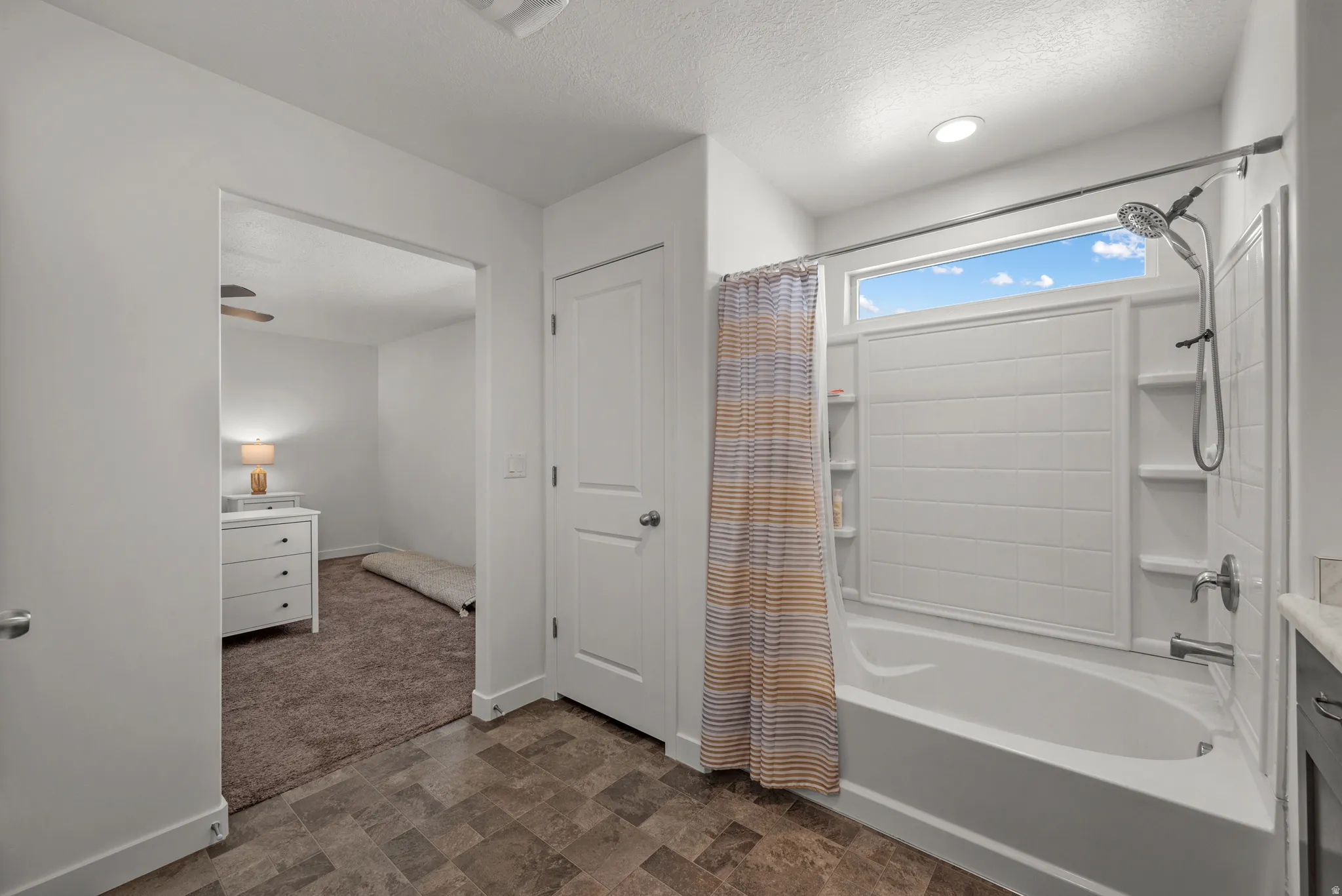 Tub/shower combination with a textured surround and built-in shelving, complemented by a transom window