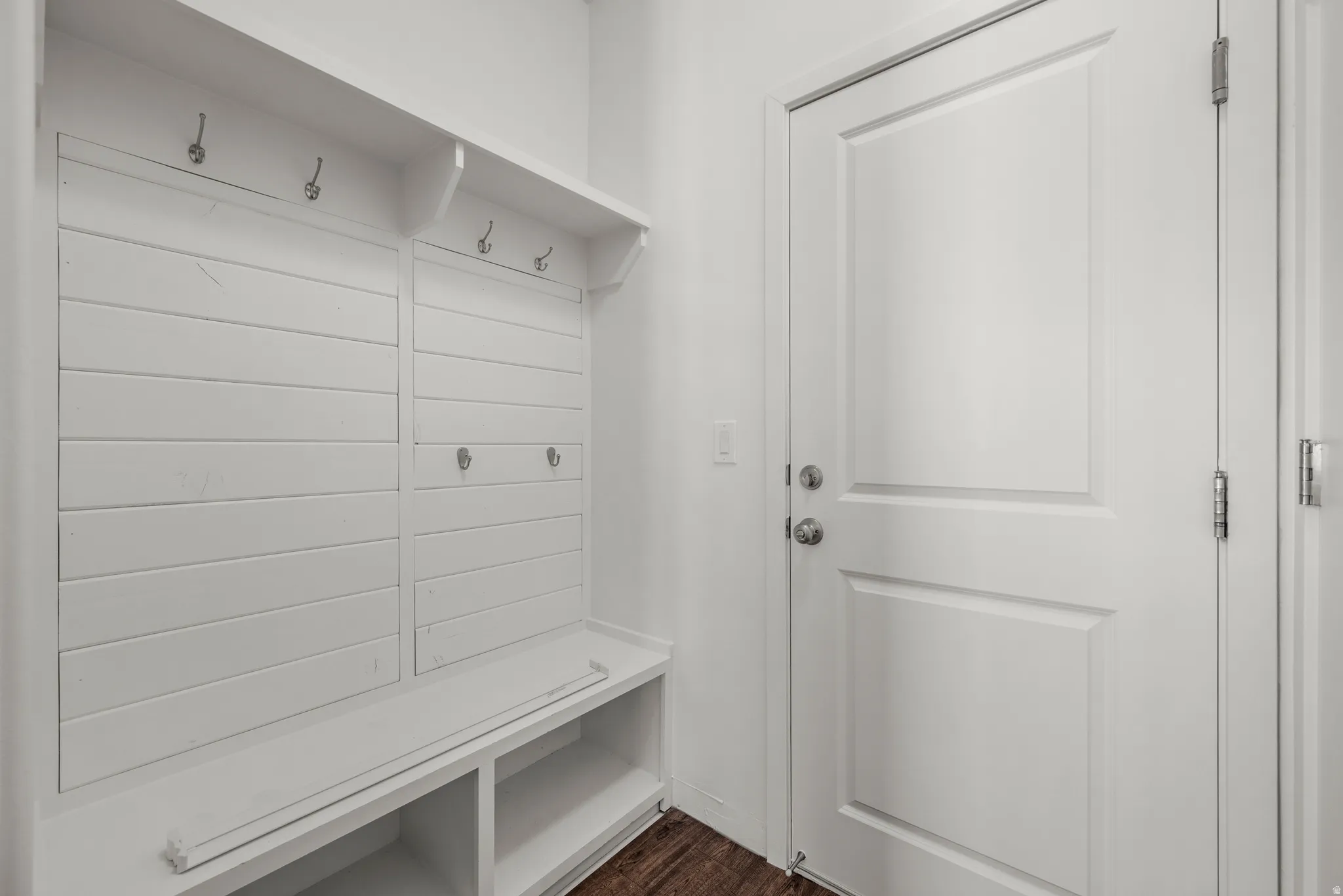 Built-in shiplap mudroom bench with coat hooks, upper shelving, and integrated storage cubbies, complemented by wood-finish flooring and a paneled interior door
