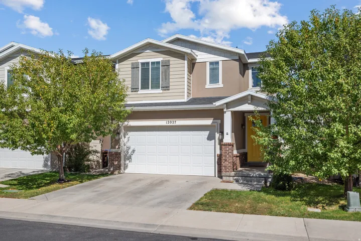 Two-story townhome with a light-colored stucco and siding exterior, an attached garage, a covered front porch with brick accents, and a bright yellow front door