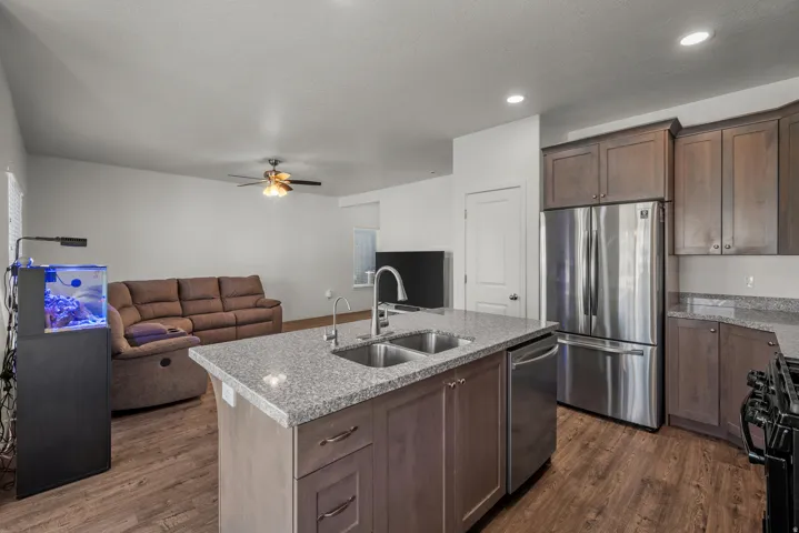 Kitchen island with a double basin sink, stainless steel appliances, wood-finish flooring, recessed lighting, and a ceiling fan