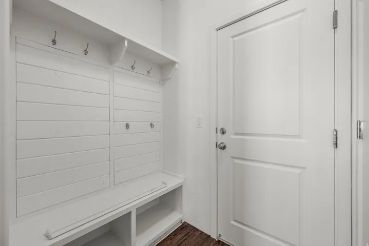 Built-in shiplap mudroom bench with coat hooks, upper shelving, and integrated storage cubbies, complemented by wood-finish flooring and a paneled interior door