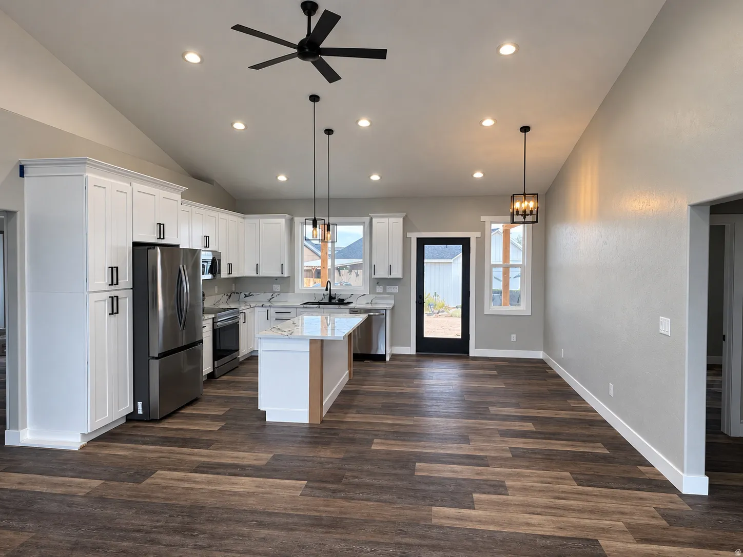 Vaulted ceiling with recessed lighting and a ceiling fan, wood-finish flooring, white cabinetry with black hardware, stainless steel appliances, and a central island with a sink