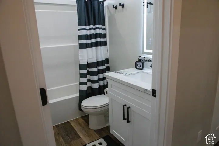 Bathroom featuring wood-finish flooring, white vanity with black hardware, white countertop, and an illuminated mirror