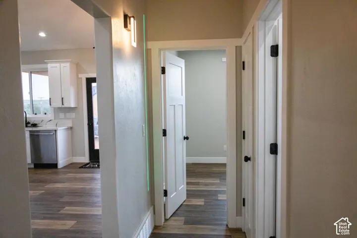 Open floor plan featuring wood-finish flooring, white shaker cabinetry, stainless steel dishwasher, and contemporary wall sconce