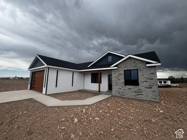 Contemporary exterior featuring stone veneer accents, vertical white siding, a wood-finish garage door, dark trim windows, and a covered entry