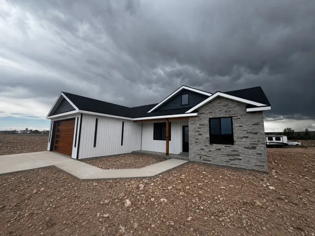 Contemporary exterior featuring stone veneer accents, vertical white siding, a wood-finish garage door, dark trim windows, and a covered entry