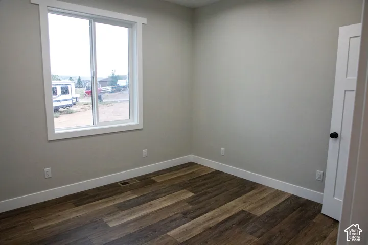 Neutral wall color, wood-finish flooring, white window trim, white baseboards, and a white panel door with a black knob