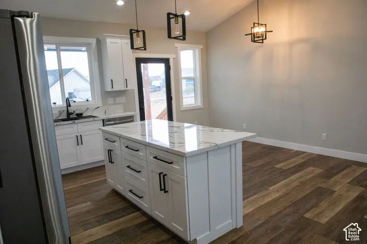 Kitchen island with a white countertop, white cabinetry with dark hardware, wood-finish flooring, and pendant lighting
