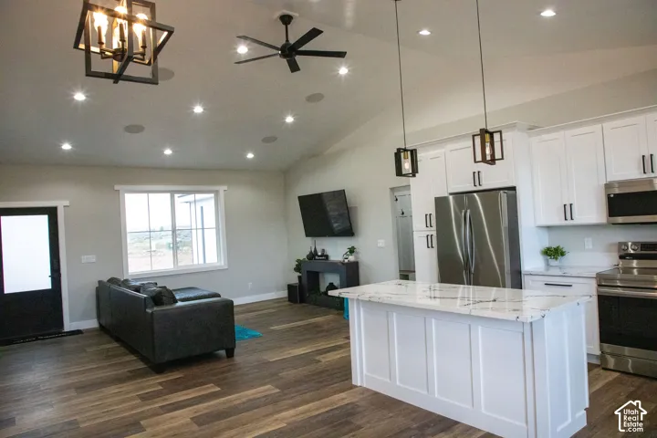 Open-concept living space with a vaulted ceiling, wood-finish flooring, recessed lighting, and a kitchen featuring white cabinetry, a kitchen island with a stone-finish countertop, and stainless steel appliances