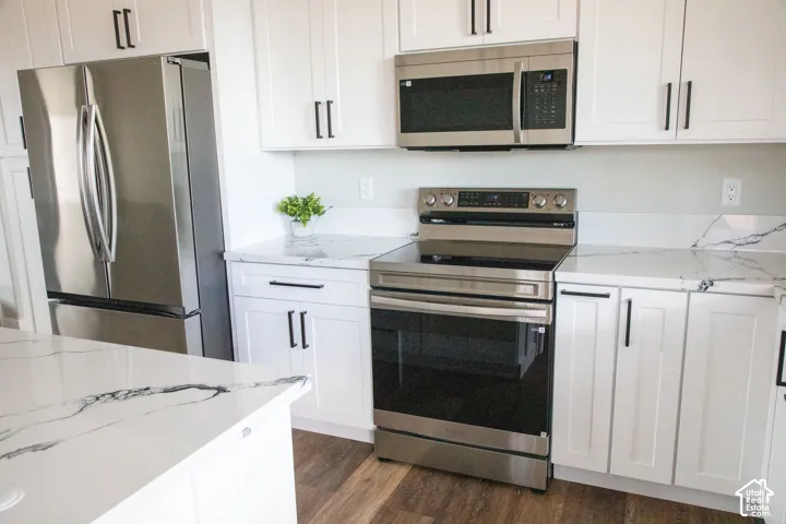 White shaker-style cabinetry with black hardware, stainless steel appliances, white countertops with dark veining, and wood-finish flooring