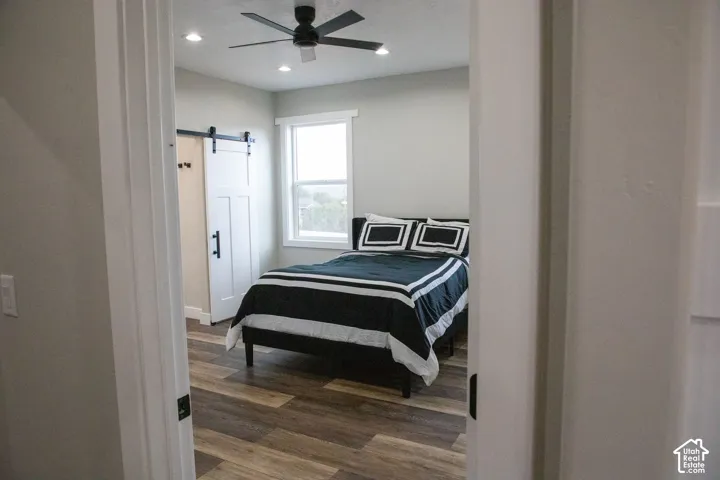 Recessed ceiling lighting, wood-finish flooring, ceiling fan, natural light window, and white barn door