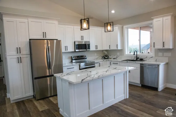 White shaker-style cabinetry with matte black hardware, stainless steel appliances, a center island with a stone-finish countertop, and wood-finish flooring