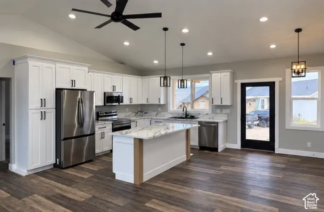 Vaulted ceiling kitchen featuring wood-finish flooring, white cabinetry, stainless steel appliances, and an island with a stone countertop
