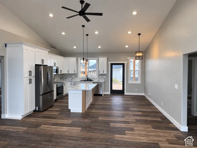 Vaulted ceiling with recessed lighting and a ceiling fan, wood-finish flooring, white cabinetry with black hardware, stainless steel appliances, and a central island with a sink