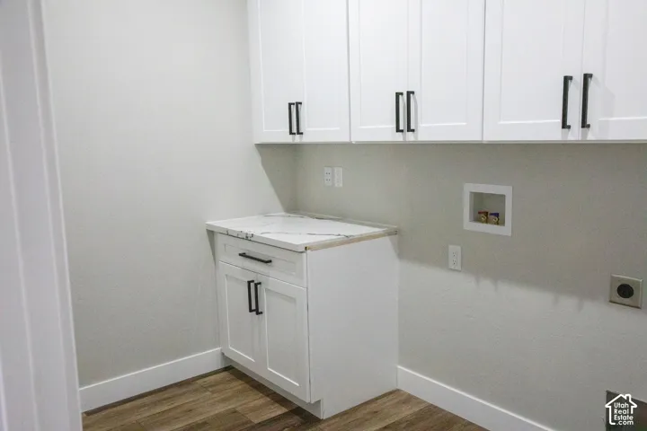 White shaker-style cabinetry with matte black hardware, wood-finish flooring, and a stone-finish countertop