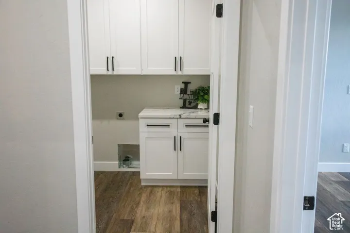 White shaker-style cabinetry with matte black hardware, wood-finish flooring, and a stone-finish countertop
