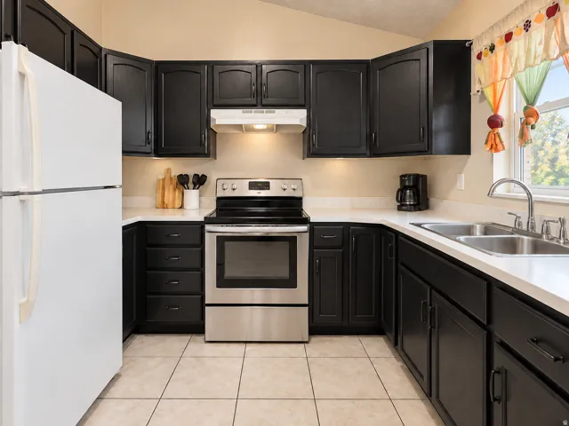 Kitchen featuring dark cabinetry, white countertops, stainless steel range, double basin sink, and tile flooring
