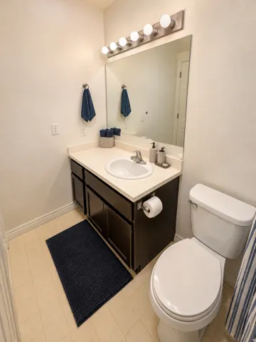 Bathroom featuring a white toilet, dark wood-finish vanity with a white countertop and integrated sink, and an overhead vanity light fixture