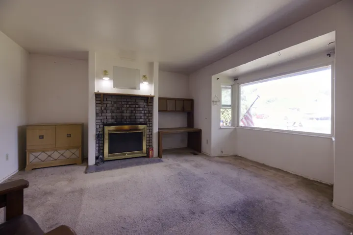 Brick fireplace with a brass-trimmed insert, built-in desk with shelving, and a large bay window