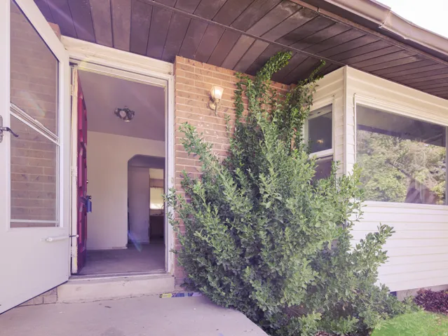 Brick exterior with a porch light fixture, wood soffit, and an entry door with a screen door