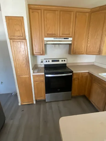 Kitchen featuring wood cabinetry, laminate countertops, a stainless steel range, and wood-finish flooring