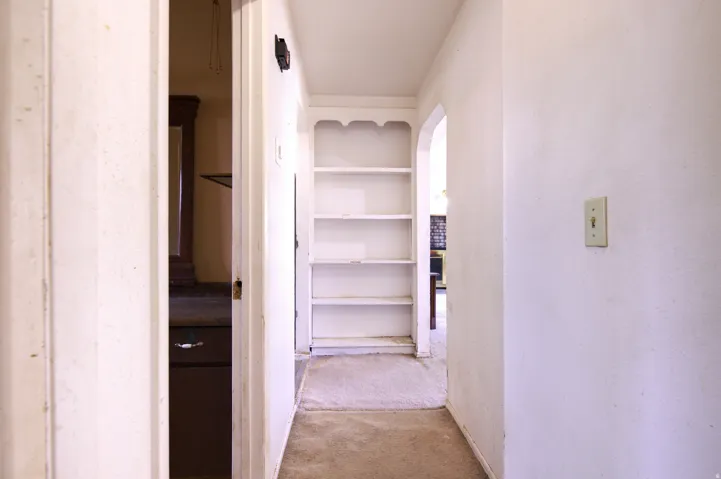 Hallway featuring a built-in shelving unit, arched doorway, and carpet flooring