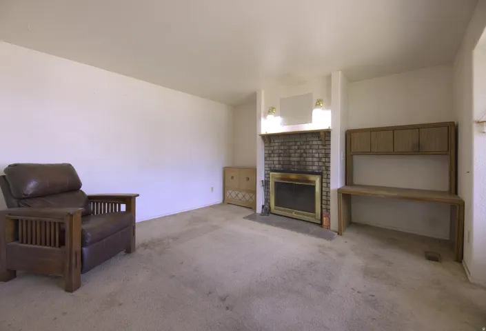 Brick fireplace with brass accents, integrated wood desk with upper cabinetry, wall-mounted light fixtures, and wall-to-wall carpeting