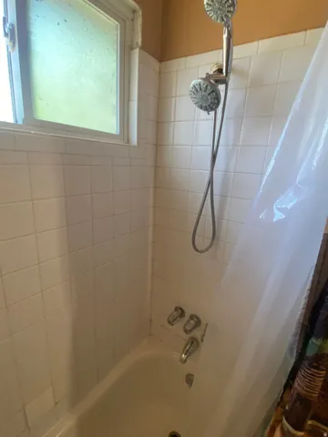 Bathtub with tile surround, dual shower heads, and an integrated window