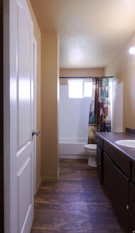 Wood-finish flooring throughout, white paneled door, and a white bathtub with subway tile surround