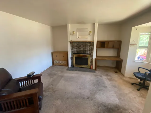 Brick fireplace with a brass firebox, built-in shelving, built-in desk, and a window with natural light